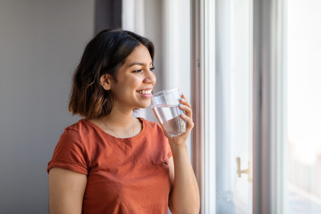 Woman drinking water in the morning and smiling while looking out window